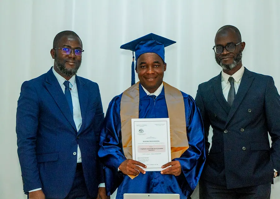 Un diplômé présente son attestation, encadré par deux enseignants